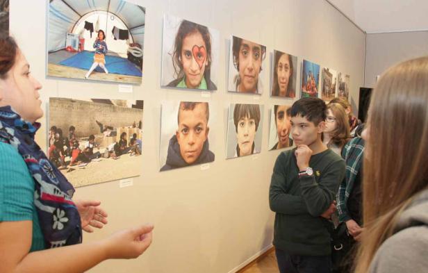 Besucher betrachten eine Fotoausstellung mit Porträts von Kindern.