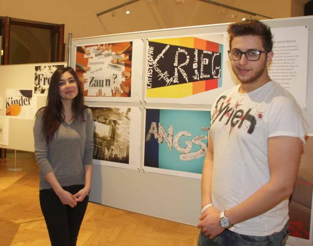 Zwei junge Leute stehen vor einer Ausstellung mit Plakaten zu den Themen Krieg und Konflikte.