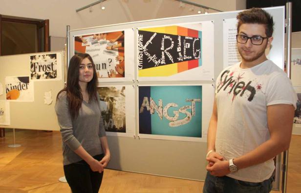 Zwei junge Leute stehen vor einer Ausstellung mit Plakaten zu Themen wie Angst und Krieg.
