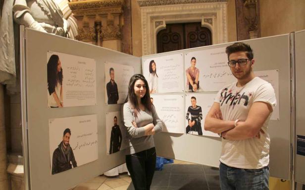 Eine Frau und ein Mann stehen vor einer Ausstellung mit Porträts und arabischer Schrift.