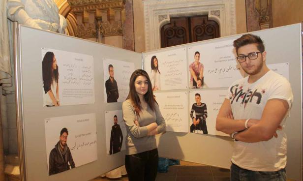 Zwei junge Leute stehen vor einer Ausstellung mit Porträts und arabischer Schrift.