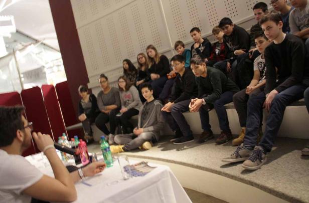 Eine Gruppe von Schülern sitzt auf einer Treppe und hört einem Redner zu.