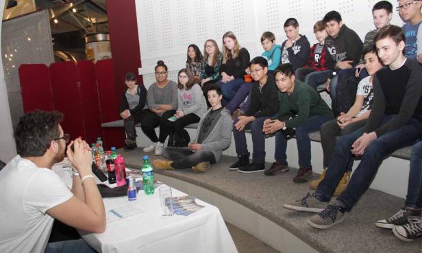 Eine Gruppe Jugendlicher sitzt auf einer Treppe und hört einem Mann zu.