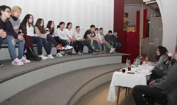 Eine Gruppe Jugendlicher sitzt auf einer Bühne und nimmt an einer Diskussion teil.