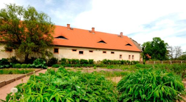 Ein langes Gebäude mit einem orangefarbenen Dach und einem Gemüsegarten im Vordergrund.