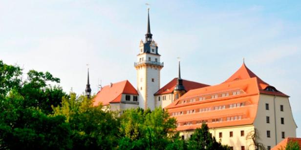 Schloss Rochlitz mit seinem markanten Turm und den roten Dächern, umgeben von Bäumen.