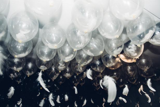 Viele transparente Ballons mit Federn darin schweben im Raum.
