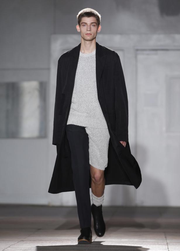 Ein Mann in einem langen schwarzen Mantel und ungewöhnlicher Kleidung läuft auf einem Laufsteg.