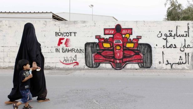 Eine Frau in traditioneller Kleidung geht mit einem Kind an einer Wand mit Graffiti vorbei, die zum Boykott der Formel 1 in Bahrain aufruft.