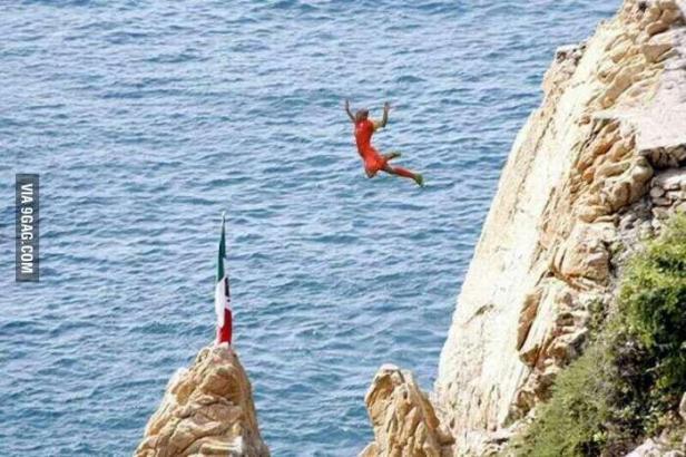 Ein Klippenspringer springt in roter Kleidung ins Meer, im Hintergrund eine mexikanische Flagge.
