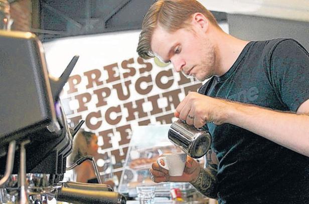 Ein Barista gießt Milch in eine Tasse Kaffee.