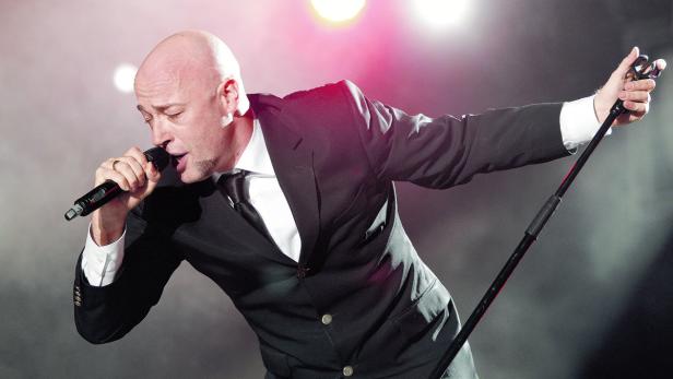 Ein Mann im Anzug singt in ein Mikrofon auf einer Bühne.