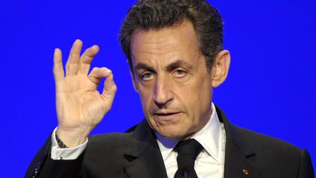 Nicolas Sarkozy gestikuliert vor einem blauen Hintergrund.
