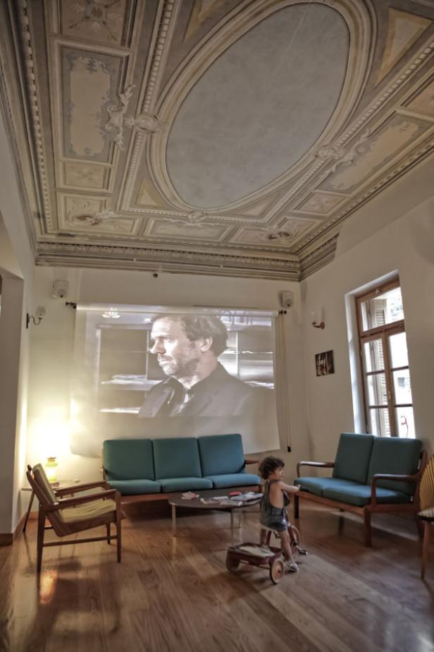 Ein Mädchen sitzt auf einem Spielzeugauto in einem Wohnzimmer, während ein Film projiziert wird.