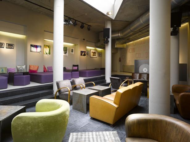 Ein Innenraum mit lila Sitzgelegenheiten auf einer erhöhten Plattform und Sesseln in verschiedenen Farben.