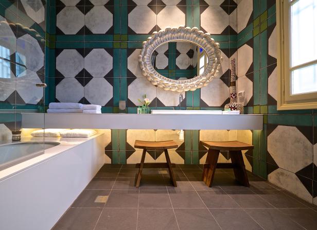 Ein Badezimmer mit gemusterten Fliesen, einem Spiegel und zwei Holzhockern.