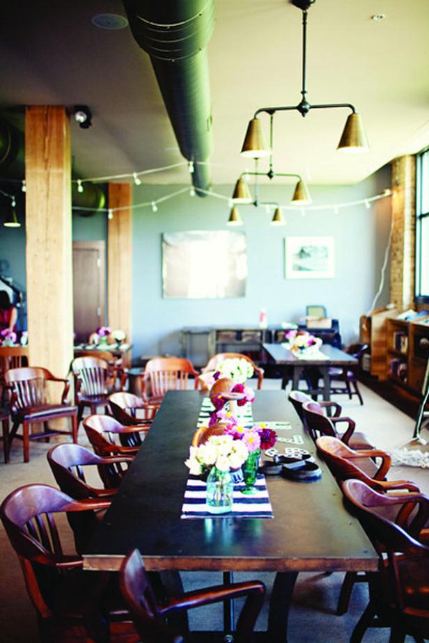 Ein langer Tisch mit Blumenarrangements und Stühlen in einem Veranstaltungsraum.