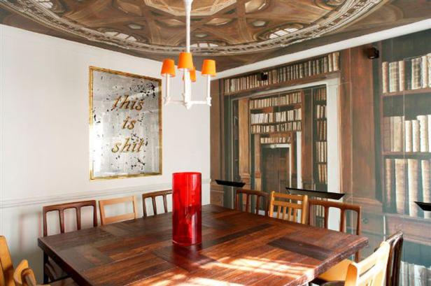 Ein Esstisch mit Stühlen, einer roten Vase und einem Spiegel mit der Aufschrift „this is shit“.