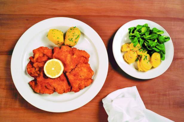 Ein Teller mit Schnitzel, Kartoffeln und Zitrone, dazu ein Teller Kartoffelsalat mit Feldsalat.