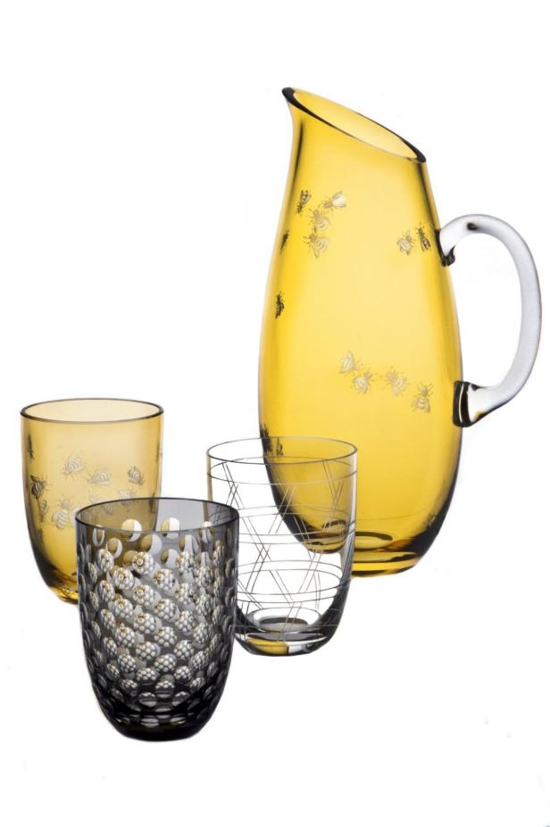 Ein gelber Krug und drei Gläser mit unterschiedlichen Mustern stehen auf einem weißen Hintergrund.
