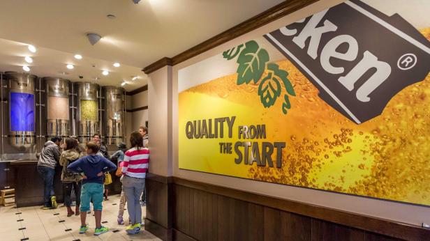 Besucher betrachten die Zutaten für Heineken in großen Behältern.