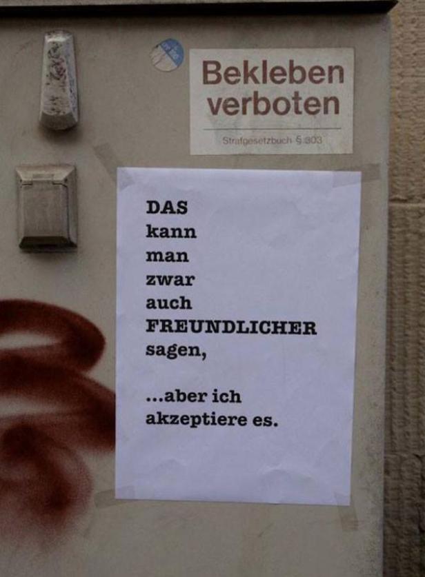 Ein Schild mit der Aufschrift „Bekleben verboten“ und ein Zettel mit dem Text: „Das kann man zwar auch freundlicher sagen, ...aber ich akzeptiere es.“.