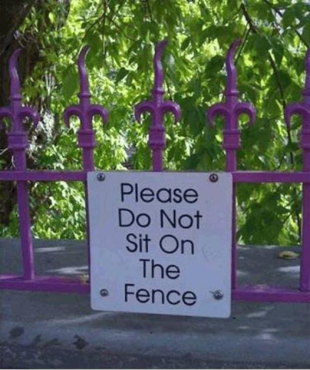 Ein Schild an einem lila Zaun fordert dazu auf, nicht auf dem Zaun zu sitzen.
