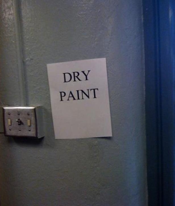 Ein Schild mit der Aufschrift „Dry Paint“ hängt an einer frisch gestrichenen Wand neben einem Lichtschalter.