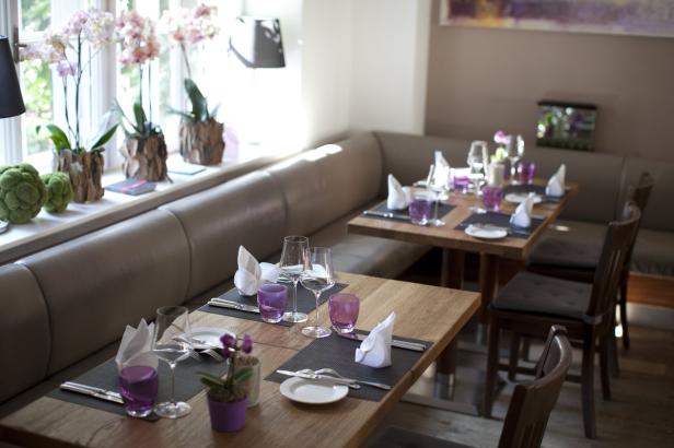 Zwei Tische in einem Restaurant sind mit Geschirr und lila Gläsern gedeckt.