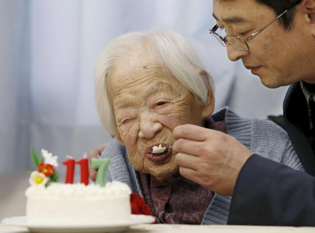 Eine 117-jährige Frau isst ein Stück Kuchen, das ihr von einem Mann gereicht wird.