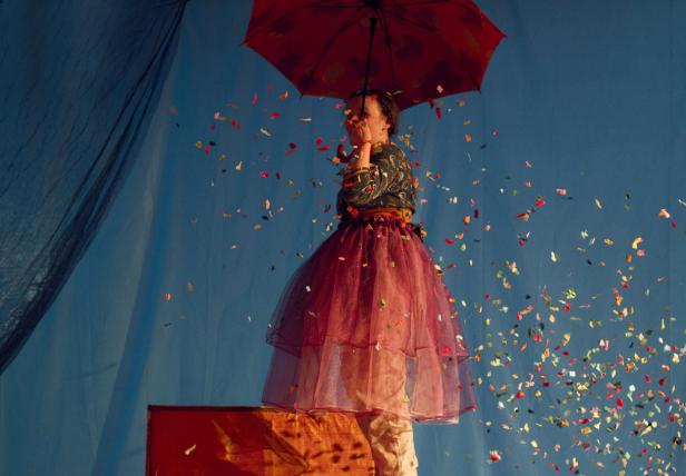 Eine Frau steht unter einem Regenschirm, während Konfetti um sie herumwirbelt.