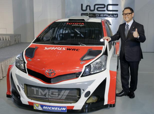 Ein Mann im Anzug posiert neben einem Toyota Yaris WRC Rennwagen.
