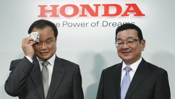 Zwei Männer in Anzügen stehen vor einem Honda-Logo.