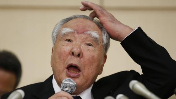 Ein älterer Mann mit Anzug gestikuliert während einer Rede in ein Mikrofon.