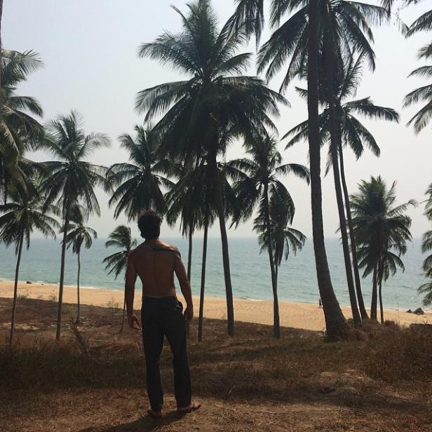 Ein Mann steht auf einer Anhöhe und blickt auf einen Strand mit Palmen.