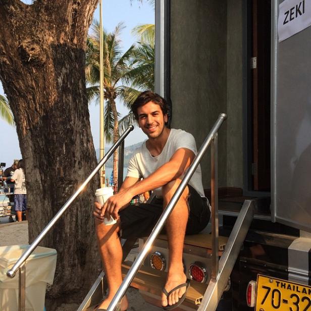 Ein Mann sitzt auf den Stufen eines Wohnwagens in Thailand und hält einen Kaffeebecher.