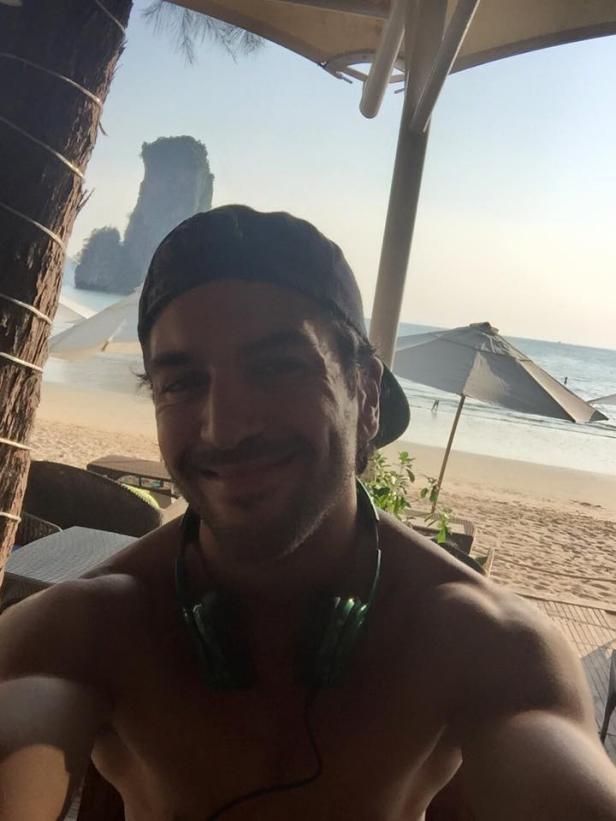 Ein Mann mit Kopfhörern macht ein Selfie am Strand.