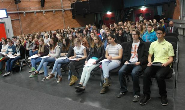 Eine Gruppe von Schülern sitzt in einem Auditorium und hält Papiere in den Händen.