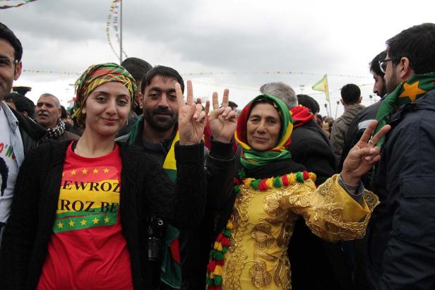 Eine Gruppe von Menschen feiert Newroz mit traditioneller Kleidung und Friedenszeichen.