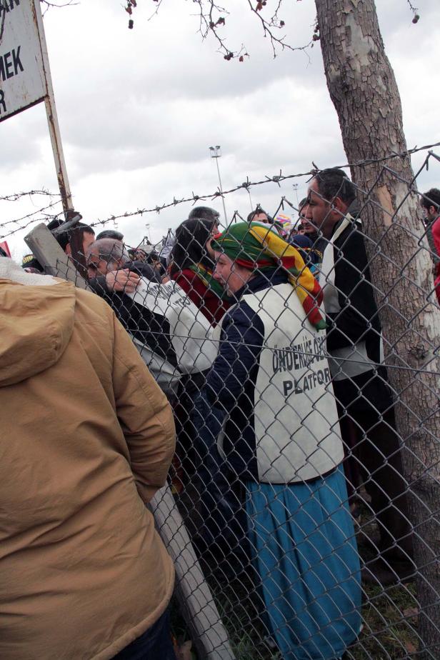 Eine Menschenmenge steht hinter einem Zaun mit Stacheldraht.