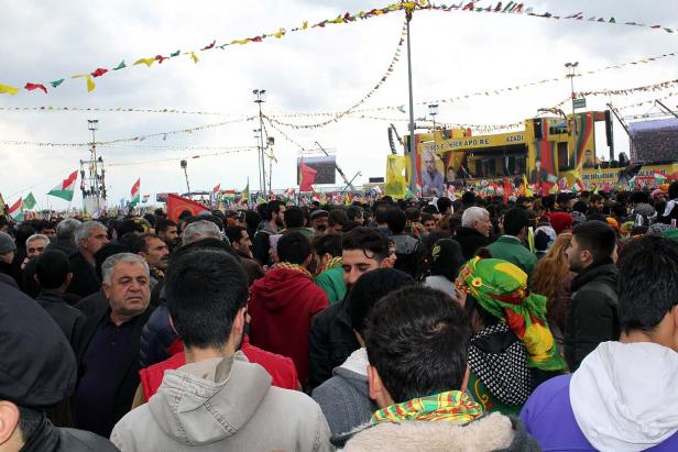 Eine große Menschenmenge versammelt sich unter kurdischen Flaggen und Bannern.