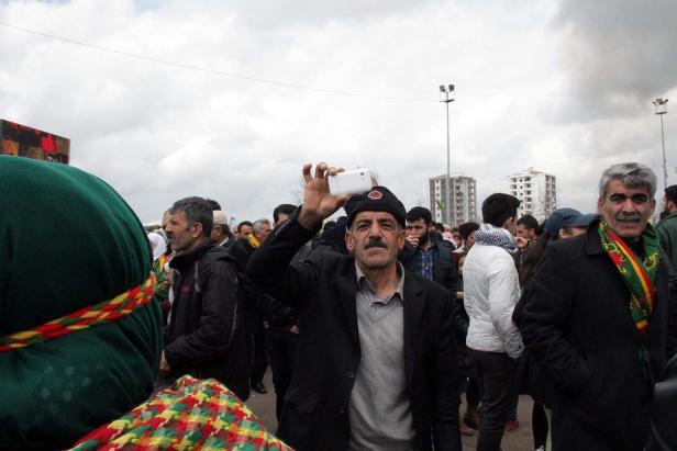 Ein Mann mit Mütze macht mit seinem Smartphone ein Foto in einer Menschenmenge.