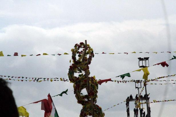 Ein mit Blumen geschmückter Maibaum unter einer Girlande bunter Flaggen.