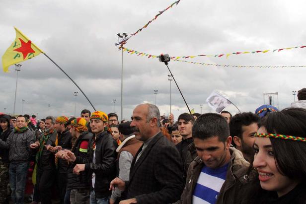 Eine Menschenmenge demonstriert mit Fahnen und Bannern unter einem bewölkten Himmel.