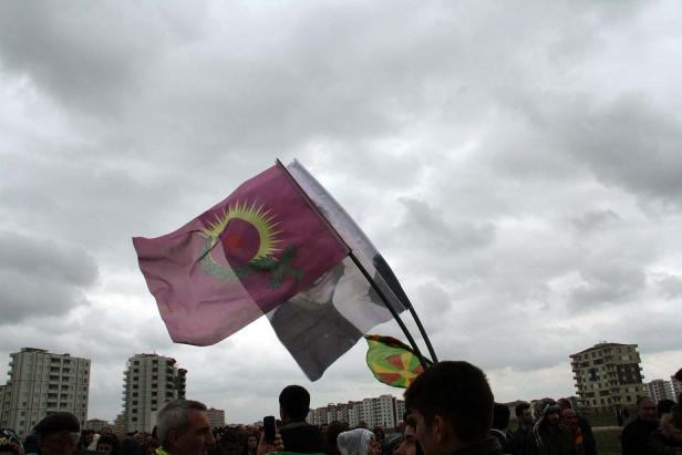 Eine Menschenmenge demonstriert mit kurdischen Flaggen vor Hochhäusern.