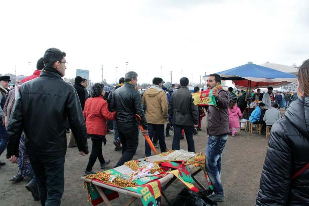 Ein belebter Markt mit Menschen und einem Stand, an dem kurdische Schals und Flaggen verkauft werden.