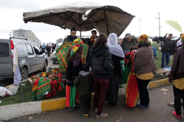 Eine Gruppe von Menschen steht an einem Stand mit kurdischen Flaggen.