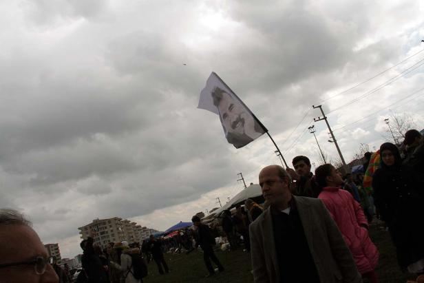 Eine Menschenmenge versammelt sich unter bewölktem Himmel, eine Fahne mit einem Porträt wird geschwenkt.