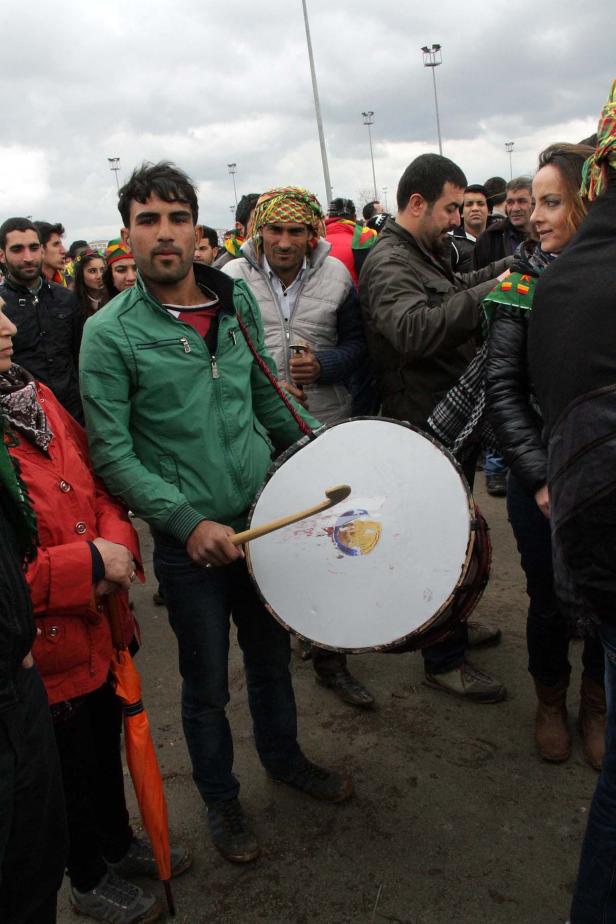 Ein Mann mit einer grünen Jacke spielt eine große Trommel in einer Menschenmenge.