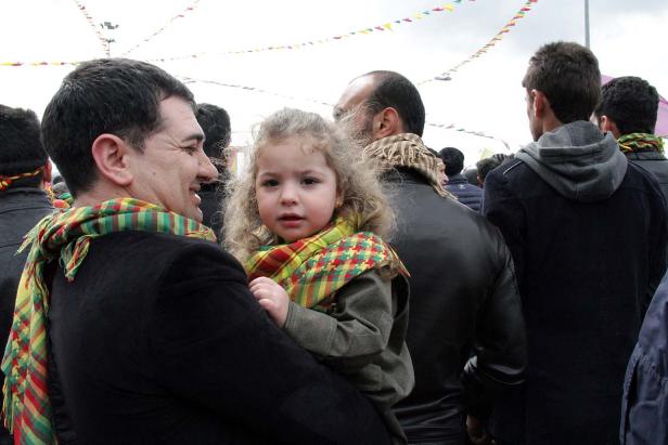 Ein Mann hält ein kleines Mädchen mit lockigem Haar auf dem Arm, beide tragen bunte Schals.